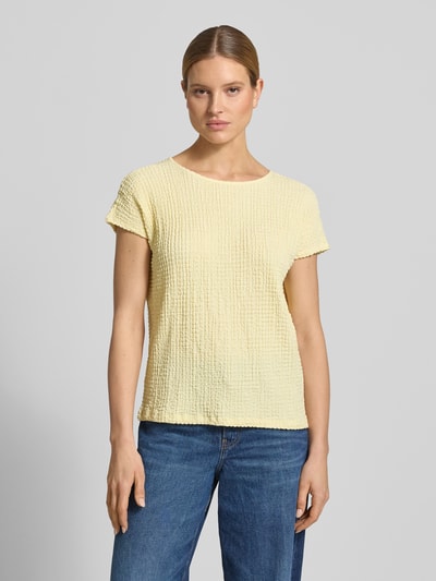 Modelka nosi Relaxed Fit T-Shirt mit Strukturmuster od s.Oliver RED LABEL, efekt: jednolity kolor, krój relaxed fit, okrągły dekolt, rękaw: krótki rękaw, wykończenie materiału: marszczenie, damski t-shirt, fakturowany wzór, jasny żółty, tekstura crinkle, widok całej sylwetki z przodu.