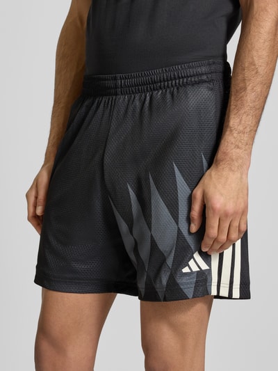 Männermodel trägt Regular Fit Shorts mit Logo-Print Modell 'Tiro' von adidas Sportswear, schwarz mit elastischem Bund, Nahaufnahme Oberkörper.