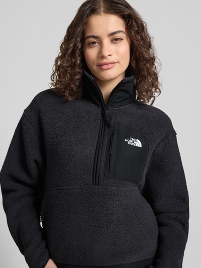 Frauenmodel trägt Fleecepullover mit Troyer-Kragen Modell 'YUMIORI' von The North Face in Schwarz mit Label-Detail, Nahaufnahme Oberkörper. Gerade Passform, elastische Abschlüsse, Rückenlänge 54 cm, Schulterbreite 51 cm, Brustweite 56 cm, Ärmellänge 58 cm.