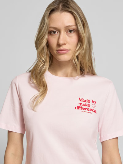 Frauenmodel trägt Regular Fit T-Shirt aus reiner Baumwolle Modell 'LUALAA EMBRO' von Armedangels in Rosa mit Rundhalsausschnitt und kurzem Ärmel, unifarben, Label-Schriftzug, Feinrippstruktur, Nahaufnahme Oberkörper.