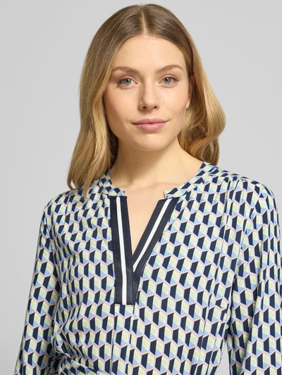 Frauenmodel trägt Regular Fit Midikleid aus reiner Viskose von Betty Barclay mit geometrischem Allover-Print, Nahaufnahme Oberkörper. Tunika-Ausschnitt, Taillierte Passform, 7/8-Arm, Abnehmbares Stoffband, Rückenlänge 99 cm, Brustweite 40 cm, Ärmellänge 47 cm bei Größe 36.