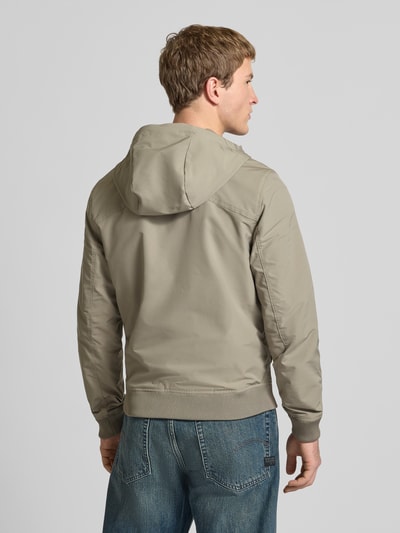 Männermodel trägt Regular Fit Jacke mit Logo-Print Modell 'Track' van G-Star Raw in beige met capuchon, steekzakken en elastische boorden, ruglengte 65 cm, schouderbreedte 41 cm, borstwijdte 48 cm, mouwlengte 67 cm, Ganzkörperansicht Rückansicht.