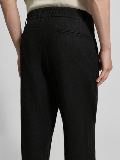 Mannenmodel draagt Tapered Fit Leinenhose mit Eingrifftaschen van MCNEAL, zuiver linnen, tapered fit, steekzakken, paspelzakken achter, ganzkörperaanzicht achteraan.