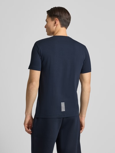 Männermodel trägt T-Shirt mit Label-Print van EA7 Emporio Armani in donkerblauw, slim fit, ruglengte 68 cm, Ganzkörperansicht Rückansicht.