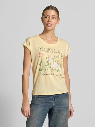 Modelka kobieca ma na sobie T-Shirt mit Motiv-Print od Christian Berg Woman, bawełniano-wiskozowy krój regular fit, żółty kolor, okrągły dekolt, długość tyłu w rozmiarze S: 54 cm, widok całej sylwetki od przodu.