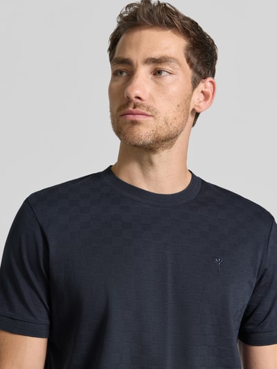 Männermodel trägt T-Shirt mit Logo-Stitching Modell 'Benluco' von JOOP! in dunklem Blau mit Strukturmuster, Nahaufnahme Oberkörper.