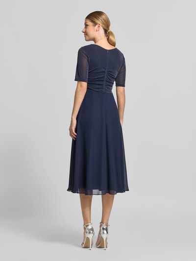 Männermodel trägt Fit and Flare Cocktailkleid mit Wasserfallausschnitt von Vera Mont in Dunkelblau mit fließender Textur, Ganzkörperansicht Rückansicht.