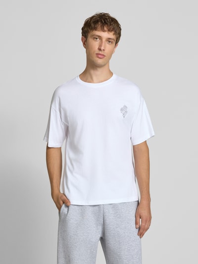Männermodel trägt Relaxed Fit T-Shirt aus reiner Baumwolle Modell "DYLAN" von JACK & JONES in Weiß mit Print-Detail, Nahaufnahme Oberkörper. Rückenlänge bei Größe M beträgt 70 cm.