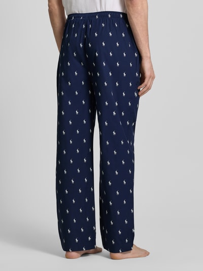Mężczyznamodel nosi Comfort Fit Pyjama-Hose aus reiner Baumwolle Modell 'PJ PANT-SLEEP-BOTTOM' von Polo Ralph Lauren Underwear, granatowe spodnie w białe wzory polo-pony, komfortowy krój, elastyczny pas ze sznurkiem, boczne kieszenie, materiał: czysta bawełna, widok całopostaciowy z tyłu.