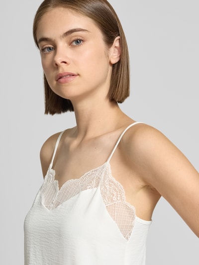 Modelka nosi białą bluzkę o luźnym kroju z obszyciem koronką, Loose Fit Blusentop mit Spitzenbesatz Model 'TIFFANY' od PIECES, zbliżenie na górną część ciała.