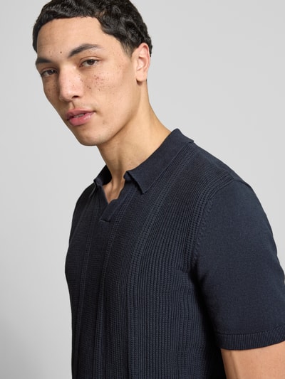 Męski model nosi Slim Fit Poloshirt in Strick-Optik Modell 'Baron' von Blend z bawełny, kołnierzyk polo, krój slim fit, imitacja dzianiny, kolor granatowy, długość tyłu w rozmiarze M 65 cm, zbliżenie na górną część ciała z przodu.