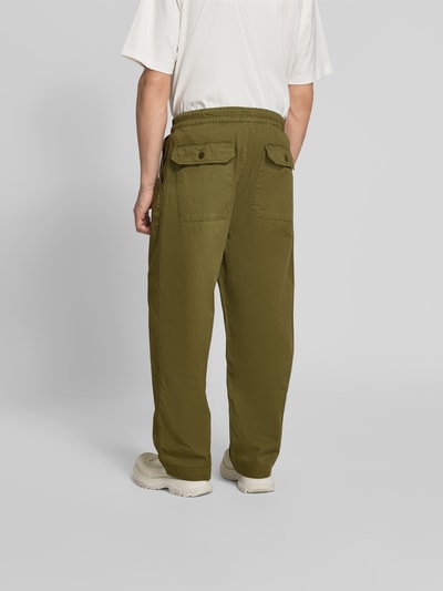 Männermodel trägt Balloon Fit Stoffhose aus Baumwolle von Officine Générale in Olivgrün mit elastischem Bund, Canvas-Textur, Ganzkörperansicht Rückansicht.