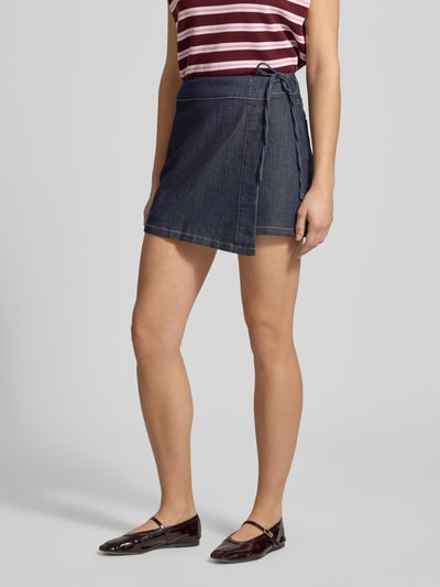 Kobiece model nosi spódnica mini z mieszanki bawełny i wiskozy, tkanina stylizowana na denim, ozdobna kokarda, model 'Swantje' od LeGer by Lena Gercke, linia a, kopertowy styl, kieszenie z tyłu, całkowita długość 38 cm, szerokość w rozmiarze 36: 35 cm. Ganzkörperansicht z przodu.