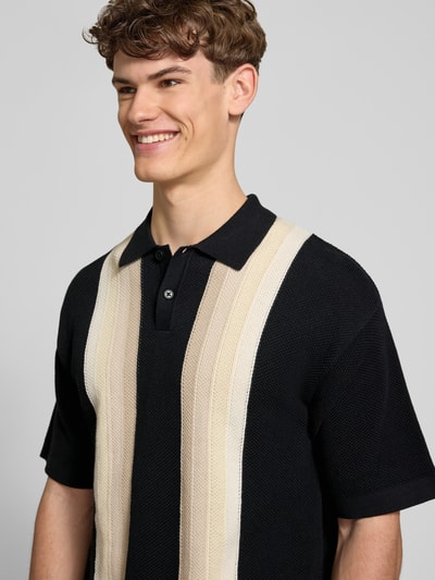 Męski model nosi koszulkę polo Relaxed Fit Poloshirt in Strick-Optik Modell 'Tellero' von Pegador z bawełny, imitacja dzianiny, krój relaxed fit, kołnierzyk polo, krótki rękaw, długość tyłu w rozmiarze M: 73 cm, czarny z beżowymi pasami, tekstura dzianiny, zbliżenie na górną część ciała, widok z przodu.