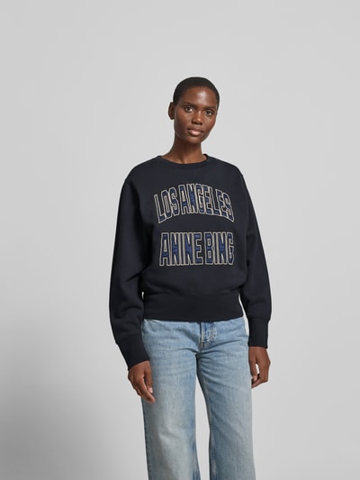Frauenmodel trägt Sweatshirt aus reiner Baumwolle von Anine Bing, dunkle Farbe, lockere Passform, Rundhalsausschnitt, Label-Detail, elastische Abschlüsse, Rückenlänge bei Größe S: 58 cm, Ganzkörperansicht von vorne.