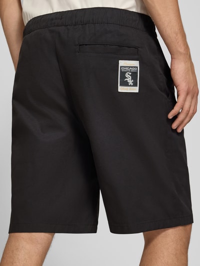 Männermodel trägt schwarze Relaxed Fit Shorts aus reiner Baumwolle von Champion, elastischer Bund, Logo-Stitching, Ganzkörperansicht Rückansicht.
