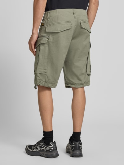 Mężczyzna nosi bermudy z mieszanki bawełny z dodatkiem streczu, model 'ROVIC ZIP' od G-Star Raw, kieszenie z patką i zamkiem, kolor khaki, 5 kieszeni, krój straight fit, zapięcie na guzik i zamek błyskawiczny, długość wewnętrzna nogawki 28 cm, szerokość w rozmiarze 32: 44 cm, widok całej sylwetki od tyłu.