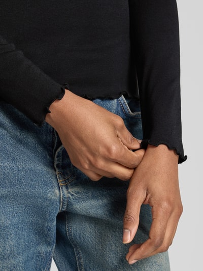 Kobiece model nosi Slim Fit Langarmshirt aus Modal-Baumwoll-Mix Modell 'Soninchen' od OPUS, czarny kolor, delikatna faktura, zblizenie na rękaw i dłoń, bluzka z długim rękawem, mieszanka modalu i bawełny, damska, detal rękawa.