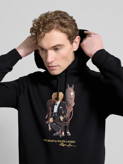 Männermodel draagt Hoodie met Labelprint van Polo Ralph Lauren in zwart katoenmix, los model, capuchon met tunnelkoord, ribboorden, nahaufnahme oberkörper.