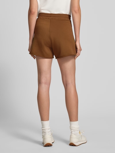 Frauenmodel trägt Sweatshorts mit Eingrifftaschen von Rich & Royal aus Baumwoll-Mix mit Stretch-Anteil, Relaxed-Fit, elastischer Bund und Tunnelzug, Innenbeinlänge 14 cm bei Größe S, einfarbig braun, glatte Textur, Ganzkörperansicht Rückansicht.