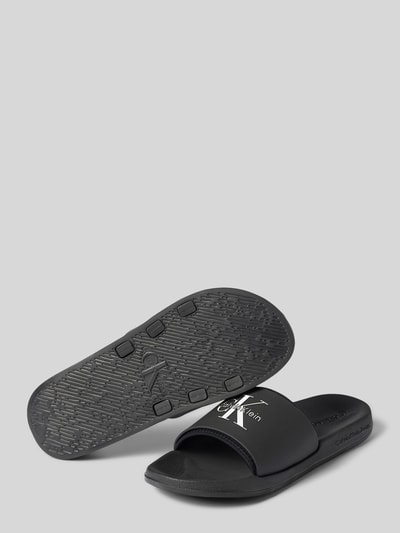 Produktfoto, czarne Badeschuhe mit Label-Prägung od CK Calvin Klein, faktura gładka, białe logo, męskie, kontekst: męskie klapki plażowe