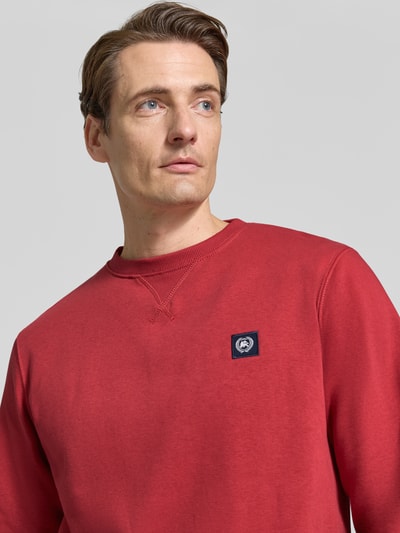 Männermodel trägt Regular Fit Sweatshirt aus Baumwoll-Mix von LERROS in Rot mit Logo-Patch, Rundhalsausschnitt, Nahaufnahme Oberkörper.