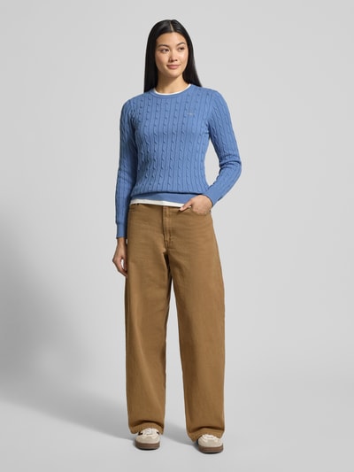 Modelka nosi Strickpullover mit Zopfmuster und Label-Stitching od Gant w kolorze niebieskim z bawełnianej mieszanki, widok całej sylwetki z przodu. Pulower o kroju slim fit, z okrągłym dekoltem, plecy 57 cm, rękaw 63 cm.