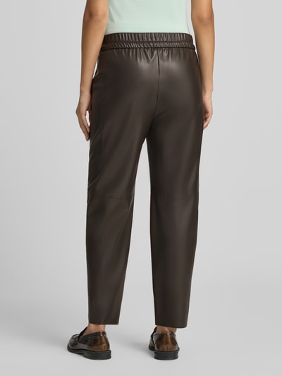 Frauenmodel trägt Tapered Fit Hose in Leder-Optik von Marc Cain, dunkelbraun, elastischer Bund, Eingrifftaschen, Ganzkörperansicht Rückansicht. Damen Hose, verkürzte Passform, glatte Textur.