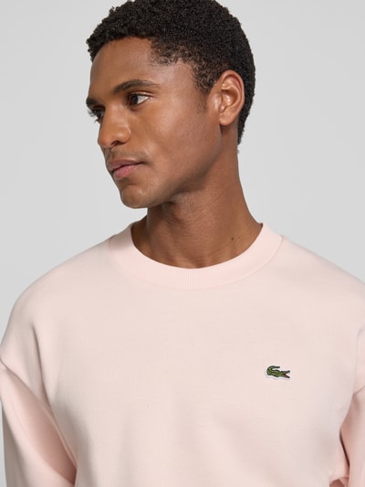 Männermodel trägt Regular Fit Sweatshirt aus Baumwoll-Mix von Lacoste in zartem Rosa, weiche Struktur, Nahaufnahme Oberkörper. Herren Sweatshirt.