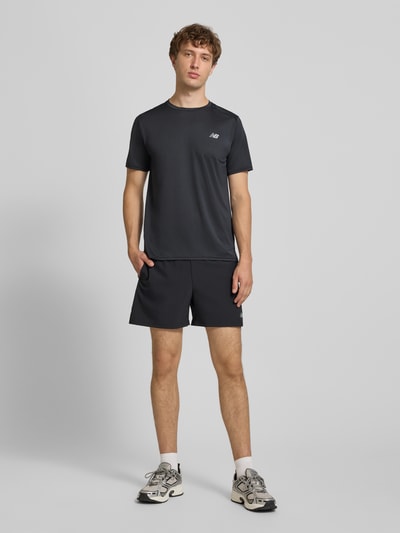 Mężczyzna nosi Funktionsshirt mit Rundhalsausschnitt und Logo od New Balance, czarny, krój regular fit, okrągły dekolt, logo, Długość tyłu w rozmiarze M: 69 cm, całkowity widok z przodu