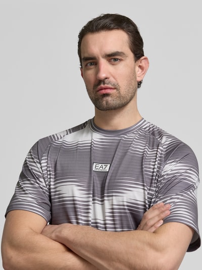 Männermodel trägt Regular Fit T-Shirt mit Logo-Applikation von EA7 Emporio Armani in Grau mit Muster, elastischer Material-Mix, Nahaufnahme Oberkörper.