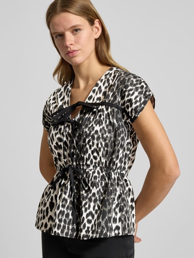 Frauenmodel trägt Blusenshirt mit V-Ausschnitt Modell 'Freya' von OH APRIL, Reine Baumwolle, Lockere-Schnitt, Schleifen-Details, schwarz-weißes Leopardenmuster, Rückenlänge bei Größe S 59 cm, Ganzkörperansicht von vorne.