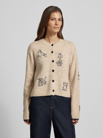 Frauenmodel trägt Strickjacke mit Stitchings und Rundhalsausschnitt von Scotch & Soda im Material-Mix mit Alpaka-Anteil, Regular-Fit, Knopfleiste, beige Farbton, Stickereien in Dunkelblau, grobe Textur, Rückenlänge 49 cm, Ärmellänge 59 cm, Ganzkörperansicht von vorne.
