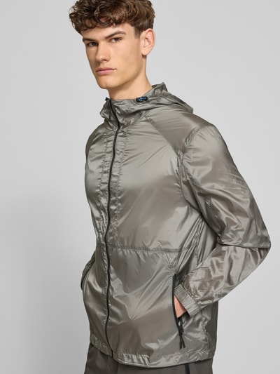 Männermodel trägt glänzende, graue Herren Jacke von HALO, Modell 'SABER JACKET 2.0' mit Reißverschlusstaschen, Kapuze, Regular-Fit, Logo, Ganzkörperansicht von vorne.
