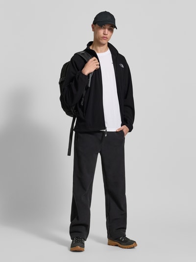 Männermodel trägt Fleecejacke mit Label-Stitching von The North Face in Schwarz, regular fit, mit rits, staande kraag, frontale Ganzkörperansicht.