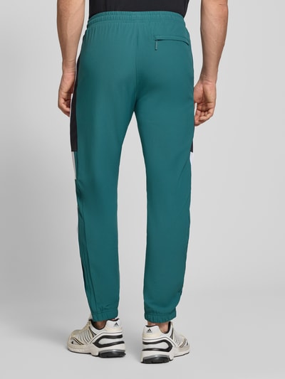 Mężczyzna nosi Sweatpants mit Logo-Stitching Modell 'CASPIO' od SERGIO TACCHINI, zielony materiał z elastycznym wykończeniem i kieszeniami, krój slim fit, całkowite ujęcie sylwetki od tyłu.