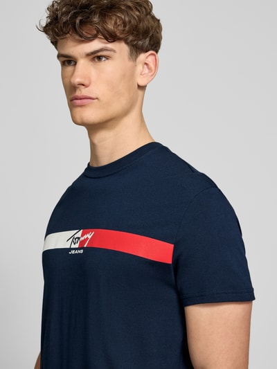 Männermodel trägt Regular Fit T-Shirt aus reiner Baumwolle von Tommy Jeans in Optik: Unifarben mit Label-Print, Jersey, Kurzarm, Nahaufnahme Oberkörper.