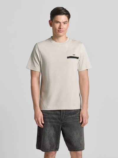 Męski model nosi t-shirt z bawełny o kroju regular fit, model 'Bobby' od Wood Wood, nadruk z logo, okrągły dekolt, widok z przodu, długość tyłu w rozmiarze M: 70 cm.