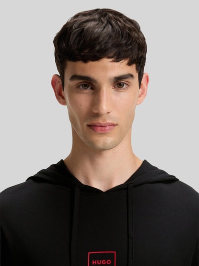 Männermodel trägt Regular Fit Hoodie aus Baumwoll-Mix Modell 'LAZE' von HUGO in Schwarz mit Label Print, Nahaufnahme Oberkörper
