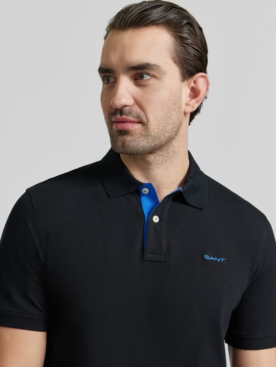 Męski model nosi Regular Fit Poloshirt mit Logo-Stitching od Gant, elastyczna mieszanka bawełny, krótkie rękawy, niebieski detal, krój regular fit, widok na górną część ciała z przodu.