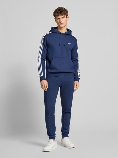 Mannelijk model draagt Sweatpants met elastische tailleband van adidas Originals, katoenmix, losse pasvorm, label-stiksel, Franse steekzakken, kleur blauw, geheel lichaamsaanzicht van voren.