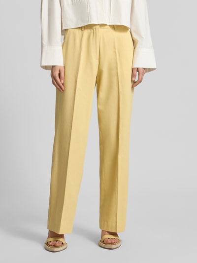 Frauenmodel trägt Wide Fit Stoffhose aus Lyocell-Mix Modell 'Edie' von Scotch & Soda in Hellgelb mit Bügelfalten und Gesäßtaschen, Nahaufnahme Unterkörper, Vorderansicht.