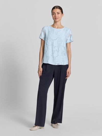 Frauenmodel trägt Blusenshirt aus Viskose-Mix mit Strukturmuster von More & More, hellblau, gerade Form, Rundhalsausschnitt, Ganzkörperansicht von vorne.