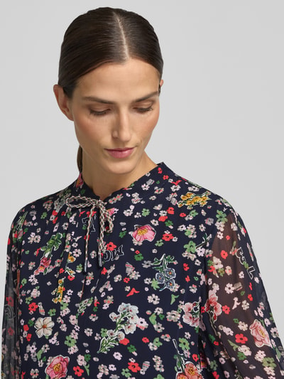 Kobiece model prezentuje sukienkę Relaxed Fit Kleid aus reiner Viskose od Marc Cain z półprzezroczystego materiału, ozdobna kokarda, długi rękaw, kwiatowy nadruk na całej powierzchni, długość tyłu w rozmiarze 36: 80 cm, szerokość w rozmiarze 36: 38 cm, długość rękawów w rozmiarze 36: 64 cm, półzbliżenie na górną część ciała.