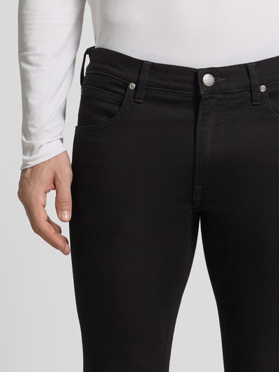 Mannenmodel draagt Slim Fit Jeans im 5-Pocket-Design Modell 'LUKE' van Lee in zwart katoenmix met stretch, nauwsluitend model, knoop- en ritssluiting, detailopname taille en bovenbeen.