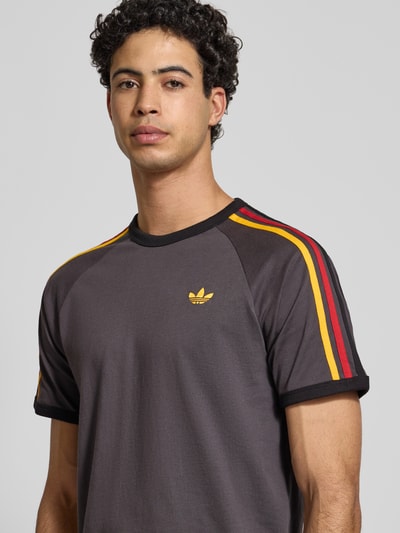 Männermodel draagt T-shirt met Labelstitching van adidas Originals in antraciet met gekleurde strepen, puur katoen, regular fit, ribboorden, ronde hals, Nahaufnahme Oberkörper. Ruglengte maat M: 73 cm.
