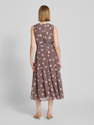 Vrouwenmodel draagt 'Midikleid mit gelegten Falten' van Christian Berg Cocktail, taupe met witte stippen, taillierte fit, katoenstructuur, zichtdichte onderjurk, afneembare stoffen ceintuur, mouwloos, ruglengte 120 cm, borstwijdte 45 cm, volledige lichaamsweergave achteraan.