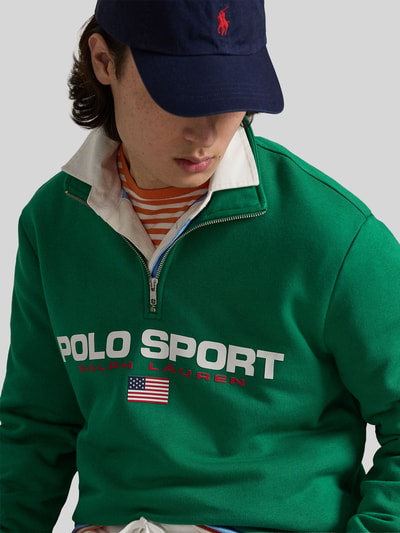 Männermodel trägt grünen Relaxed Fit Troyer aus Baumwoll-Mix von Polo Ralph Lauren mit Label Print, kurzem Reißverschluss, Nahaufnahme Oberkörper.