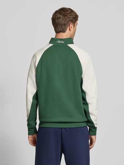 Männermodel trägt Relaxed Fit Sweatshirt aus Baumwoll-Mix von Nike in Dunkelgrün mit weißen Ärmeln, glatte Textur, Ganzkörperansicht Rückansicht.