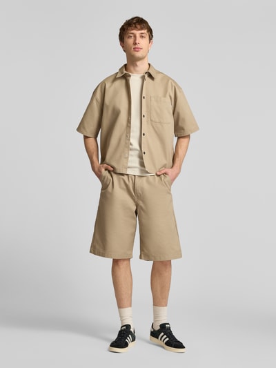 Männermodel trägt Relaxed Fit Freizeithemd mit Brusttasche von REVIEW, Material-Mix mit Baumwoll-Anteil, Kentkragen, Knopfleiste, 1/2-Arm, sandfarben, glatte Textur, Ganzkörperansicht von vorne.
